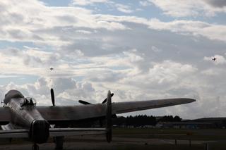 The Lancaster bomber on the  tarmac at Bournemouth Airport  while the Red Arrows fly overhead.   