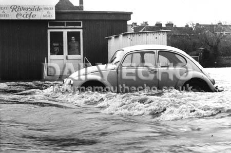 A car caught by rapid rising flood water on the Ham car park, Blandford watched by the proprieter of the Riverside Cafe after a storm in 1974.