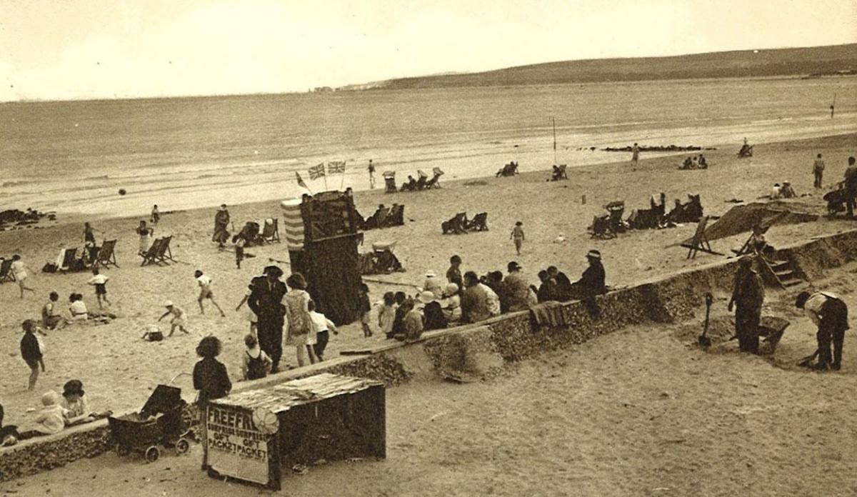 An undated photochrom letter card showing Sandbanks beach. Note Punch and Judy and the group getting ready to watch in the centre and free gifts on stall in front. Submitted by Ken Mart.
Made by Photochrom Co Ltd based in Kent