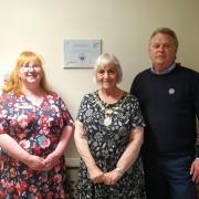 Sue Wiffen, Cllr Anne Filer and Iain Slack, stand next to the newly received EMBRACE Dementia Accreditation at Red Admiral View.
