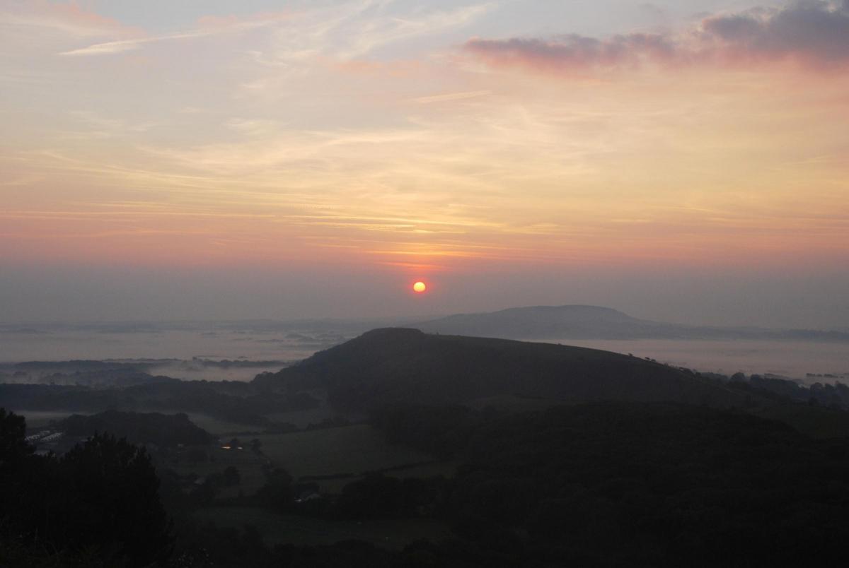 Sunrise  over the Purbeck Hills, with mist in the valley of Poole Harbour and Rempstone Forest, left, and the valley of Harmans Cross and Swanage, right. Taken  by Ben Buxton